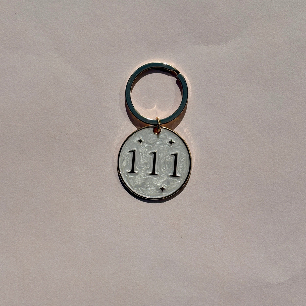 Silver metal keyring with engraved 111 angel number on pale pink background
