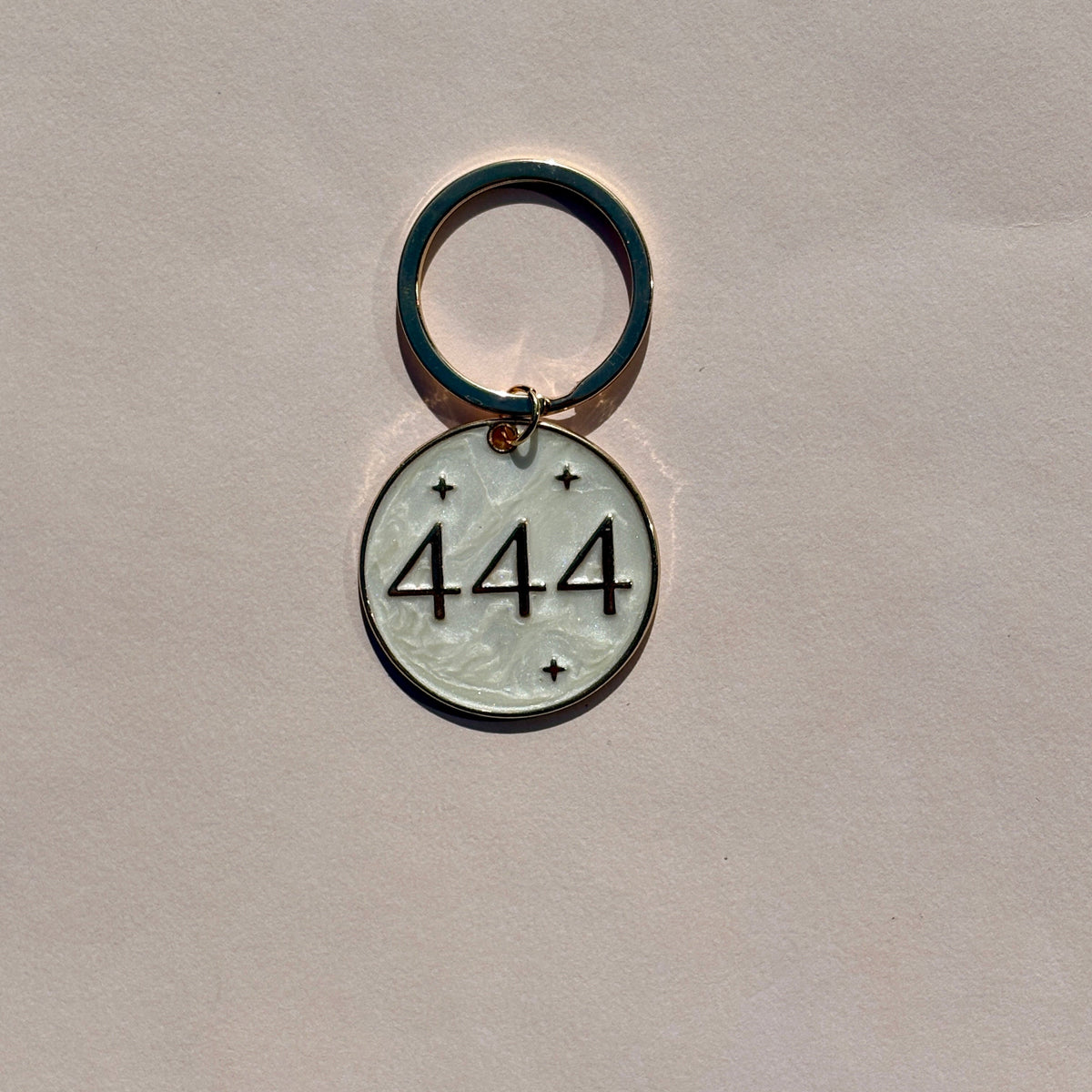 Silver metal keyring with engraved 444 angel number design on pale pink background