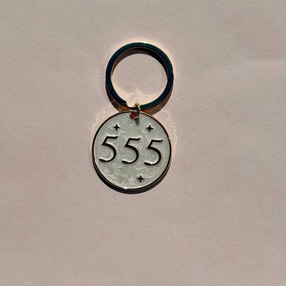 Silver metal keyring with engraved 555 angel number design on soft pink background