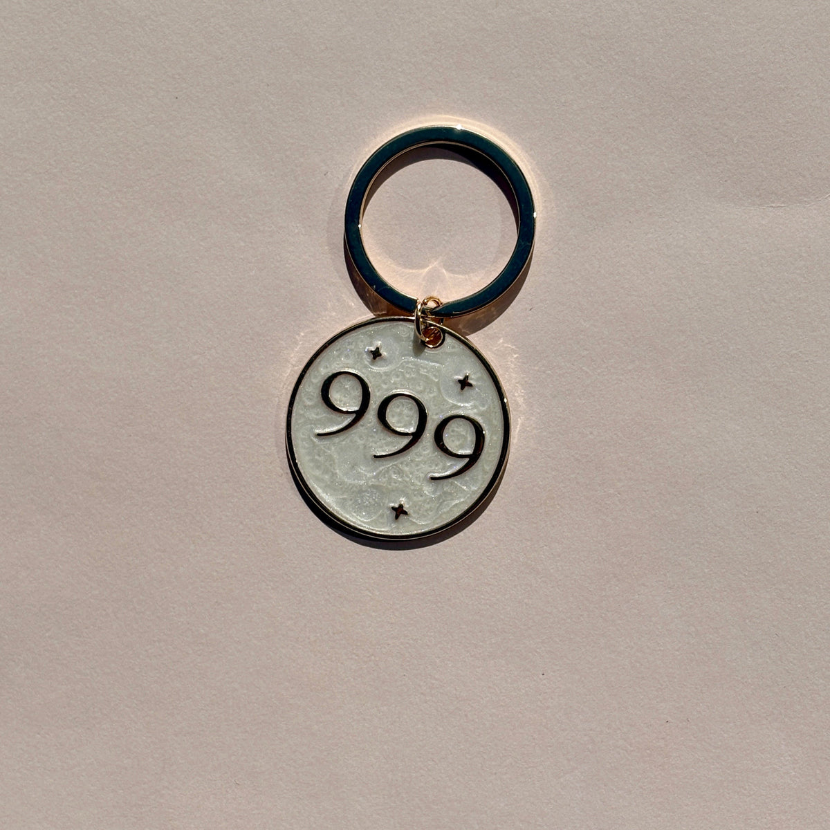Silver metal keyring engraved with 999 angel number on soft pink background