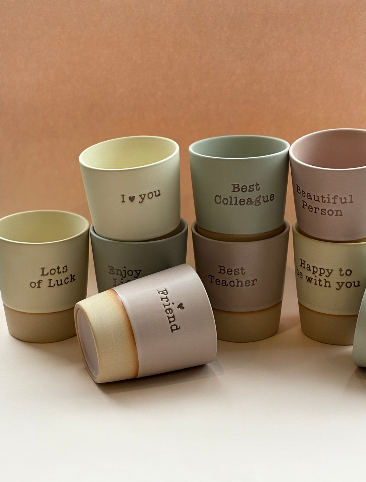 Set of affirmation ceramic cups with various messages on a beige background