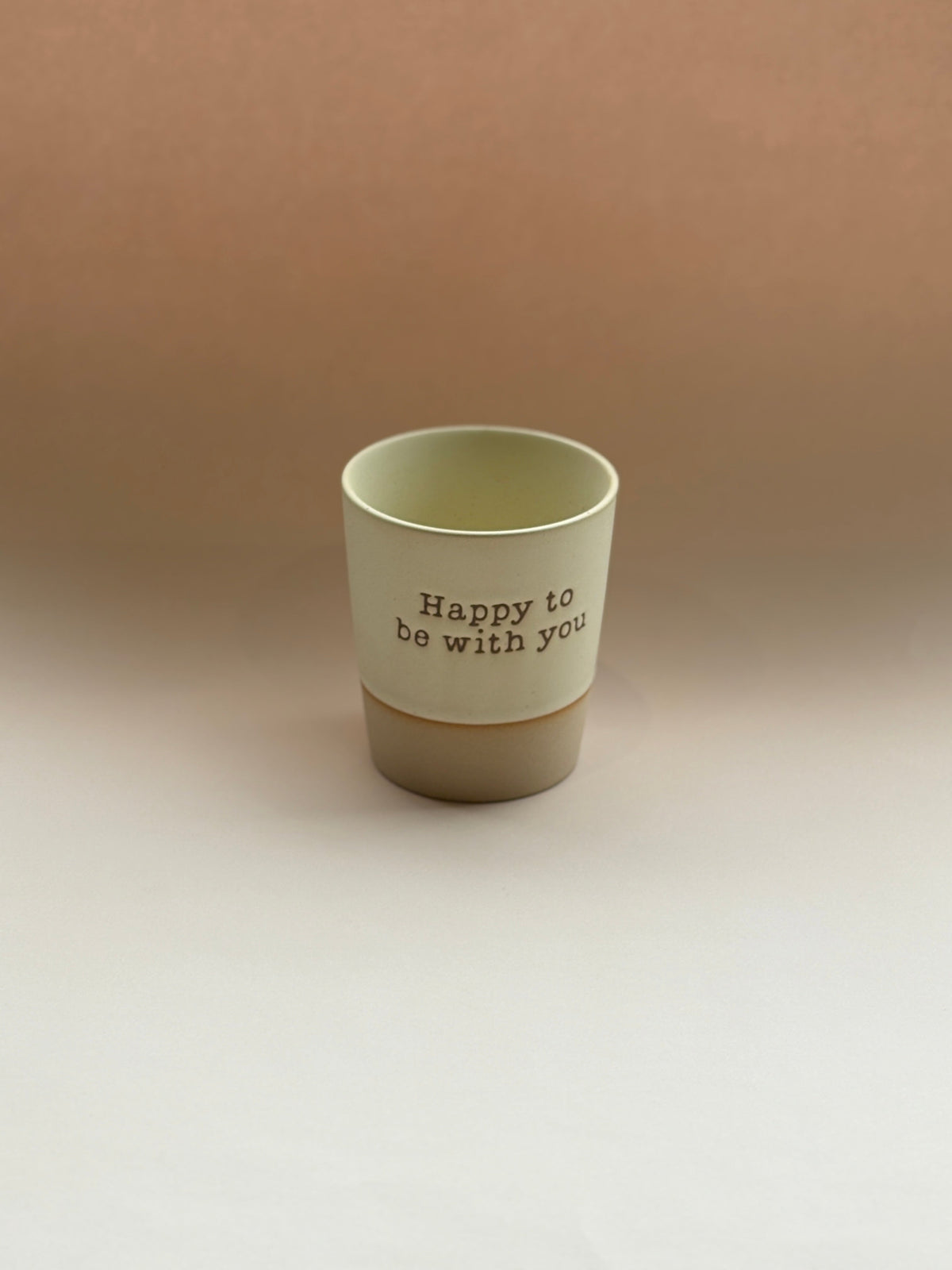 Beige ceramic cup with 'Happy to be with you' text on a beige background