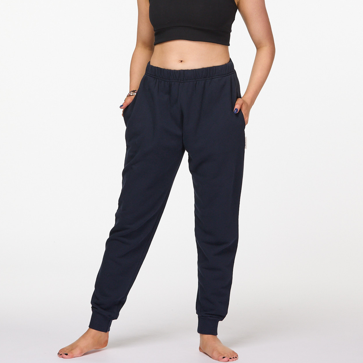 Woman wearing navy organic cotton tapered pants with black sports bra barefoot on white background