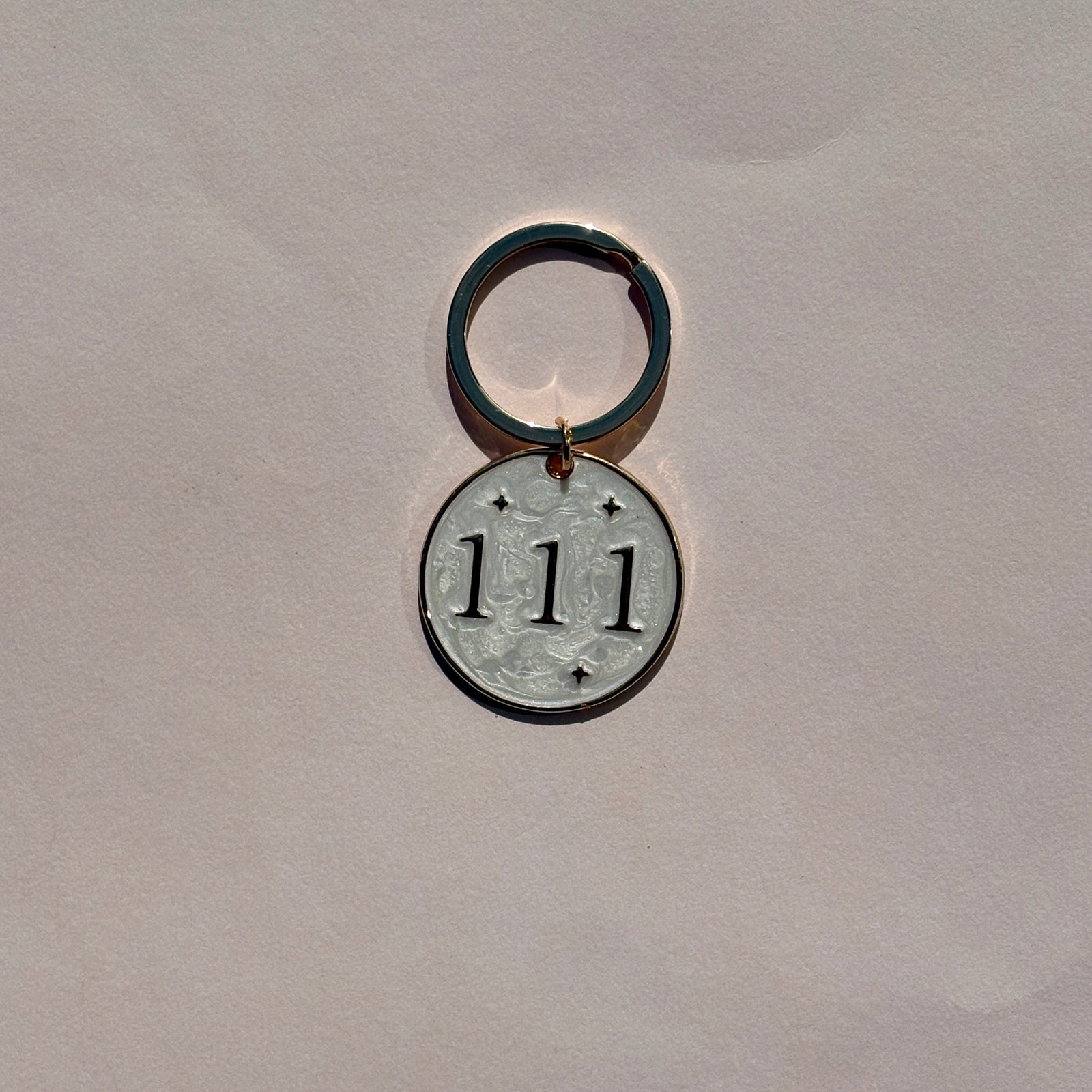Silver metal keyring with engraved 111 angel number on pale pink background