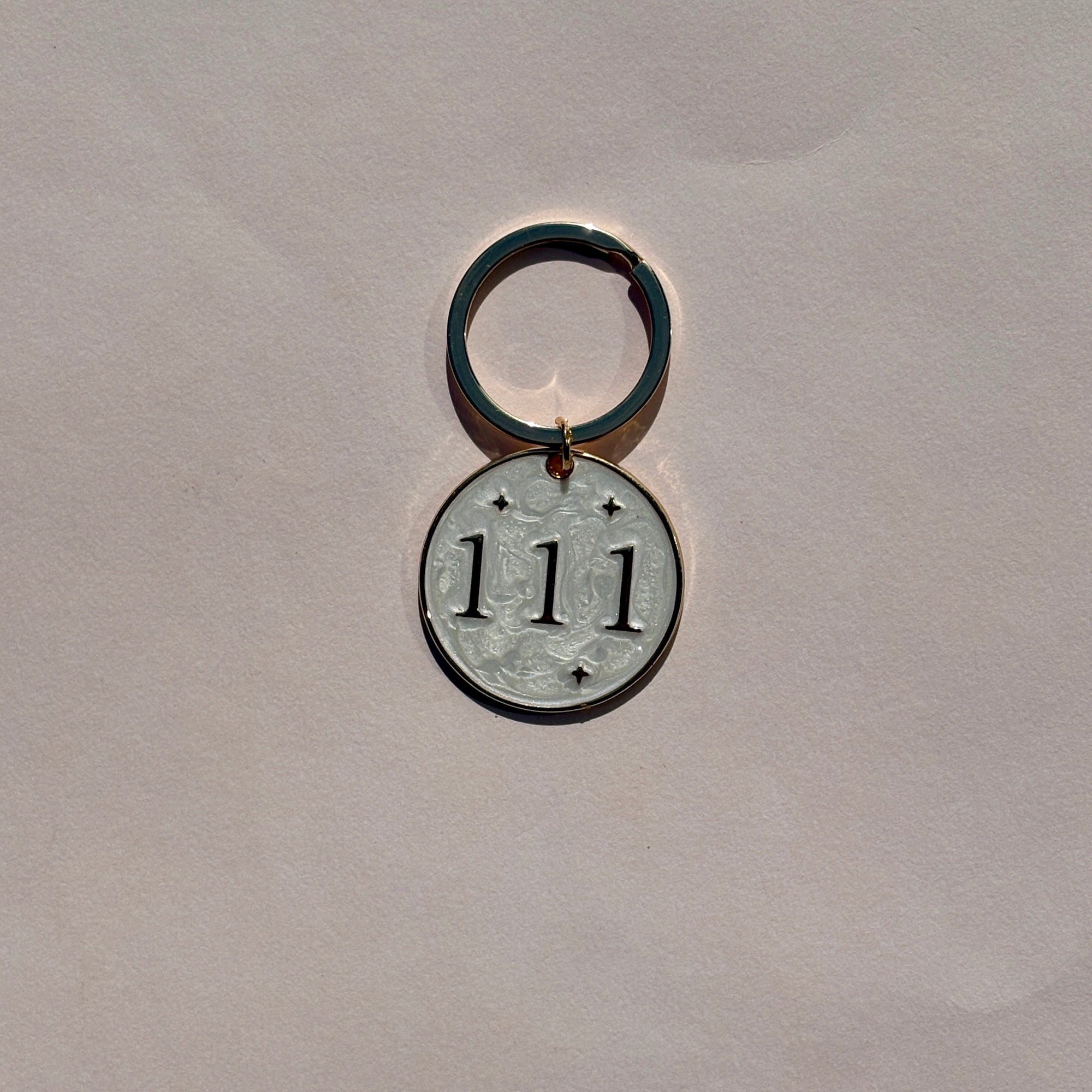Silver metal keyring with engraved 111 angel number on pale pink background