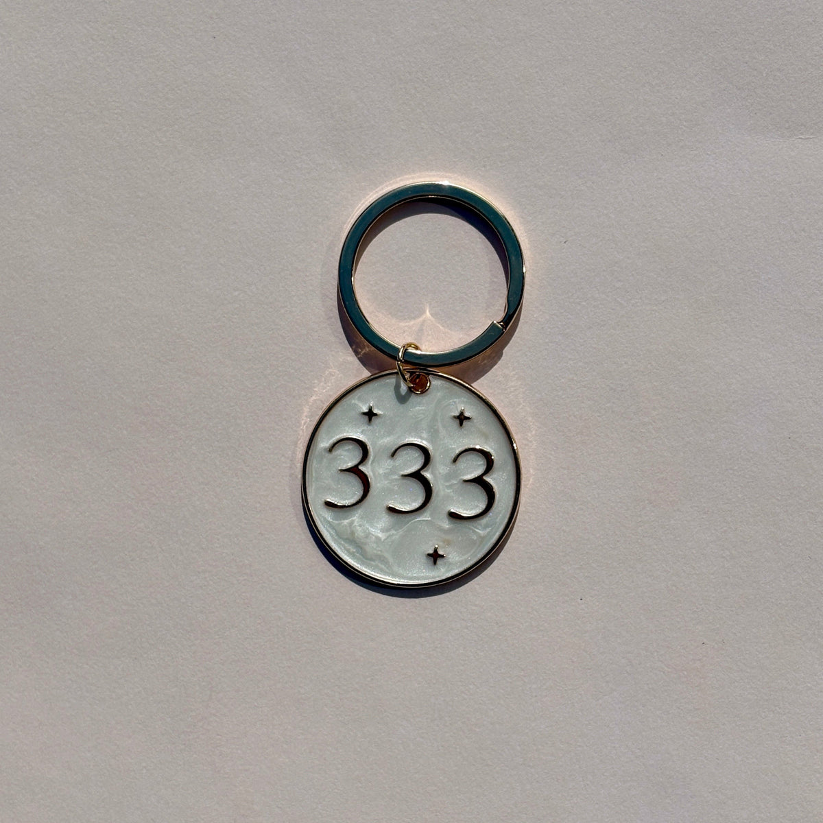 Silver metal keyring with engraved 333 angel number design on soft pink background