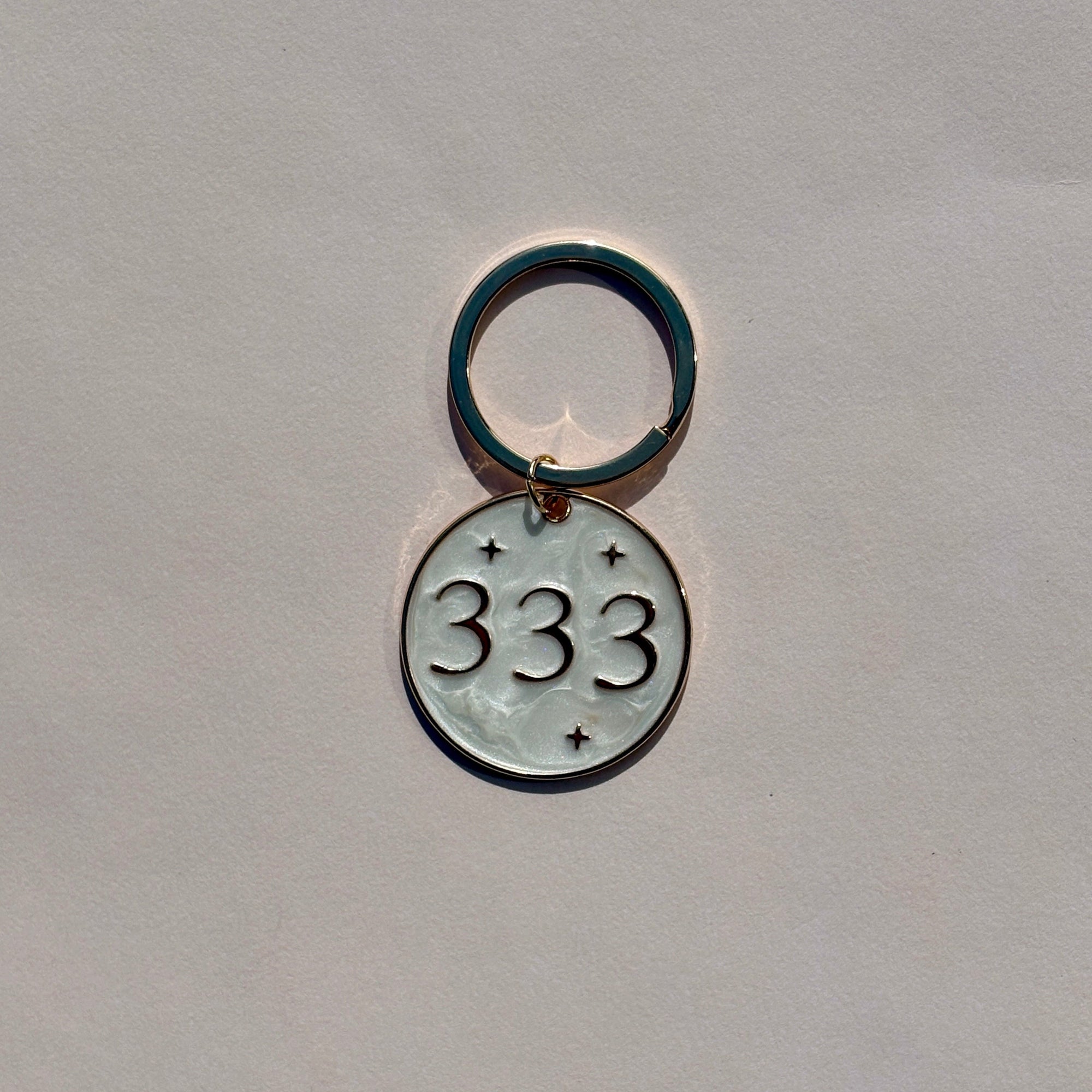 Silver metal keyring with engraved 333 angel number design on soft pink background