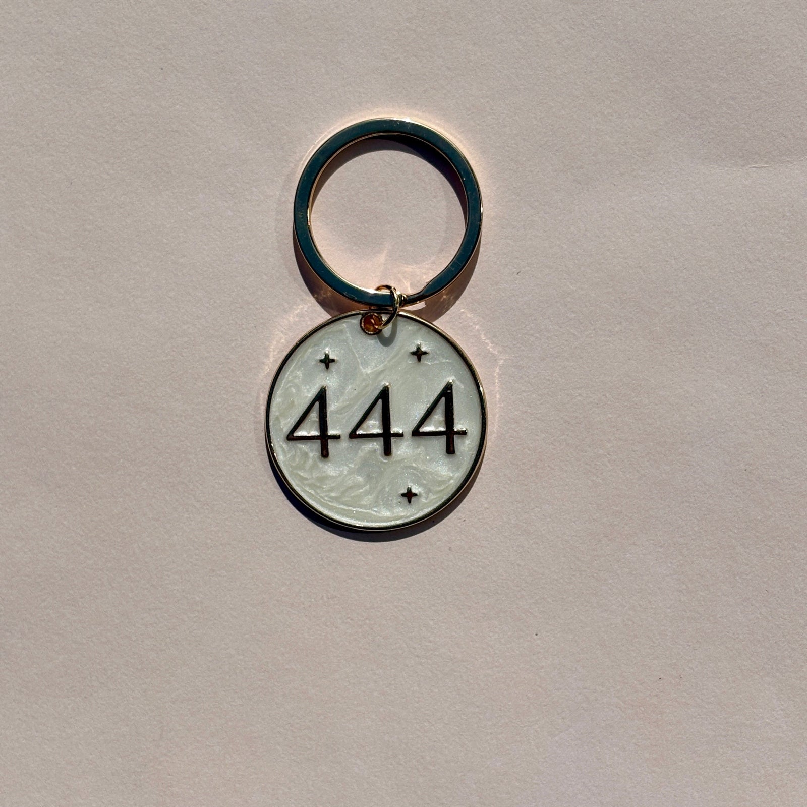 Silver metal keyring with engraved 444 angel number design on pale pink background