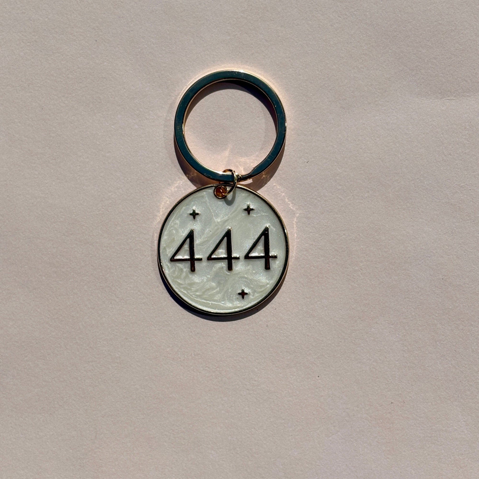 Silver metal keyring with engraved 444 angel number design on pale pink background