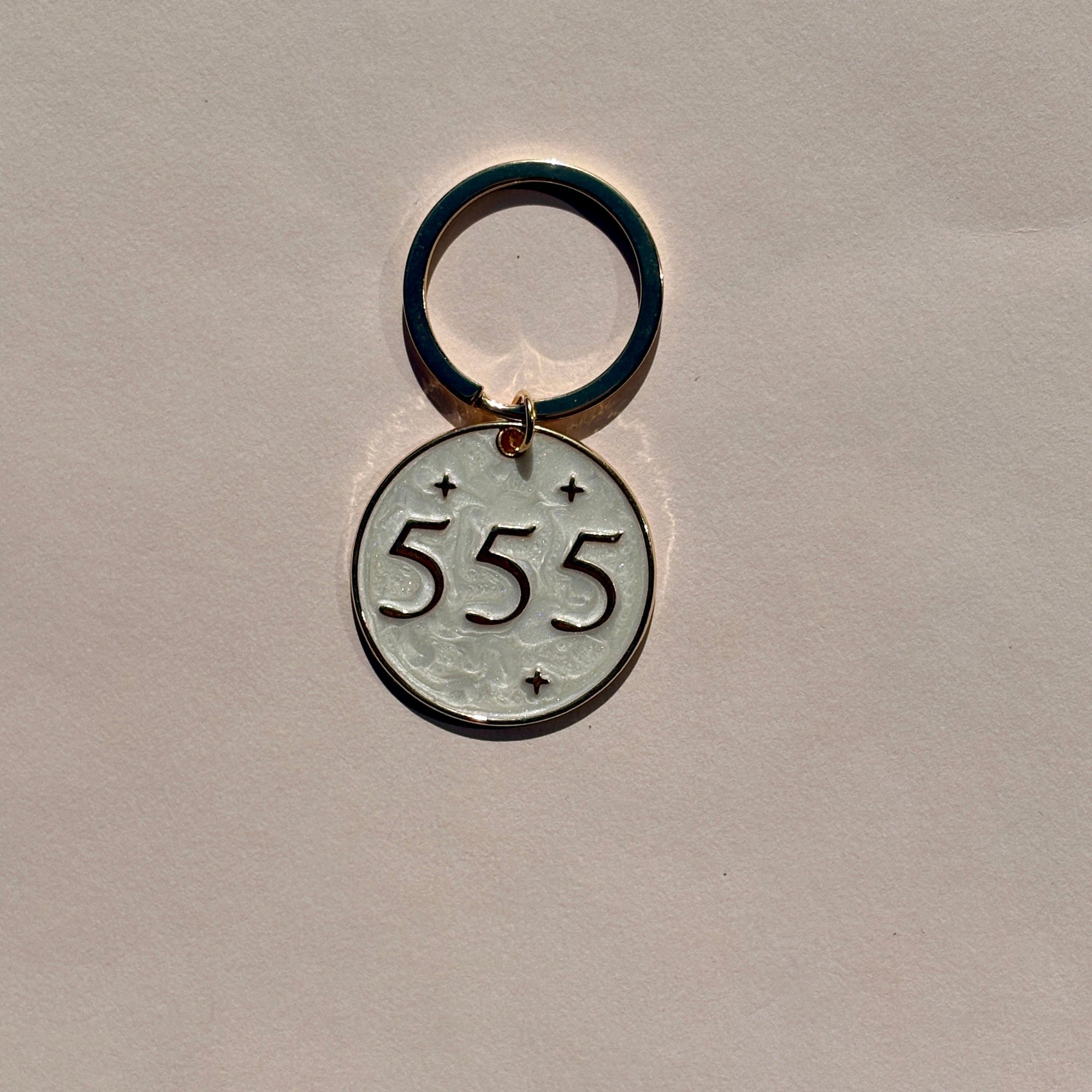 Silver metal keyring with engraved 555 angel number design on soft pink background