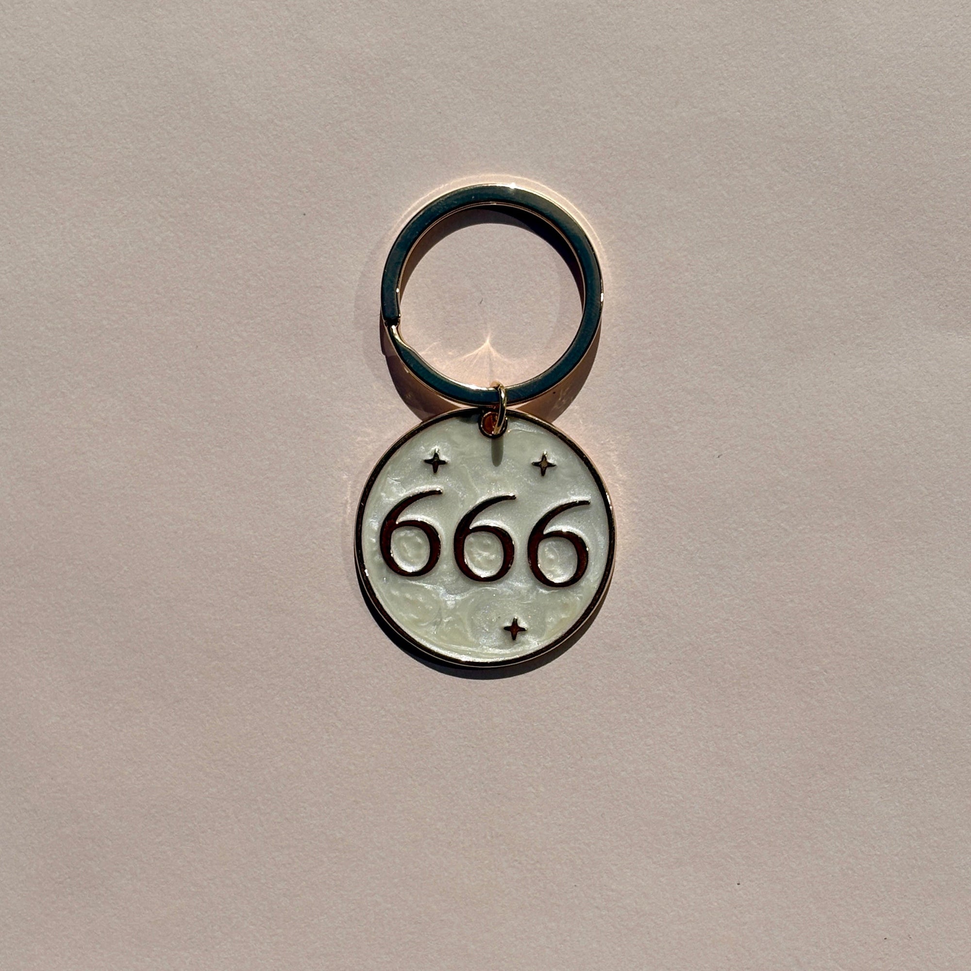 Silver metal keyring engraved with 666 angel number on soft pink background