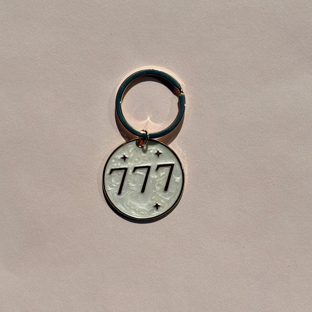 Silver metal keyring engraved with 777 angel number on soft pink background