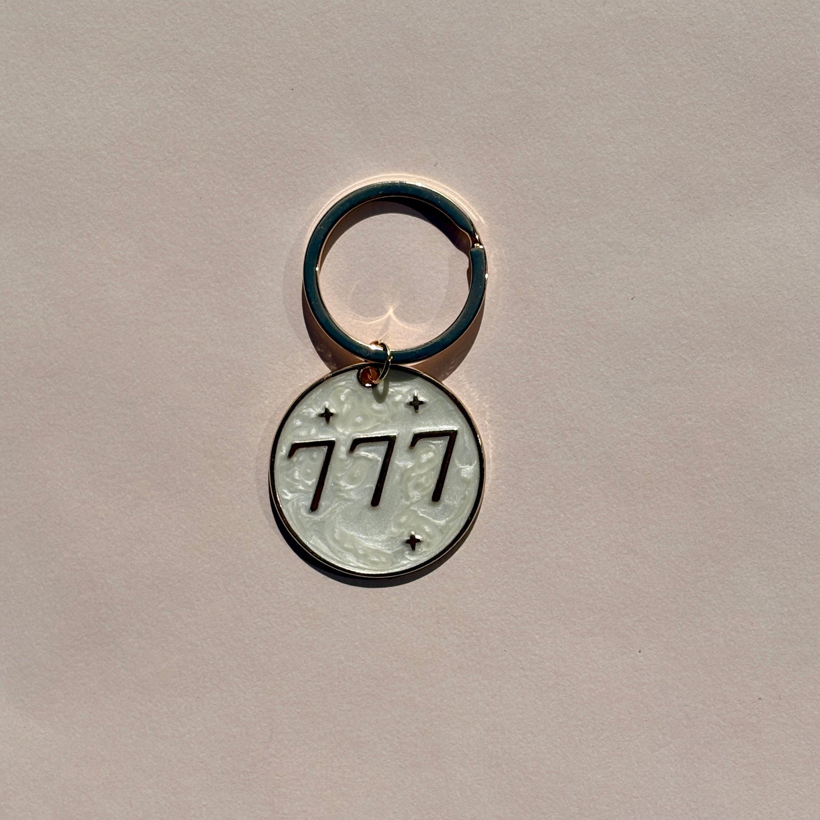 Silver metal keyring engraved with 777 angel number on soft pink background