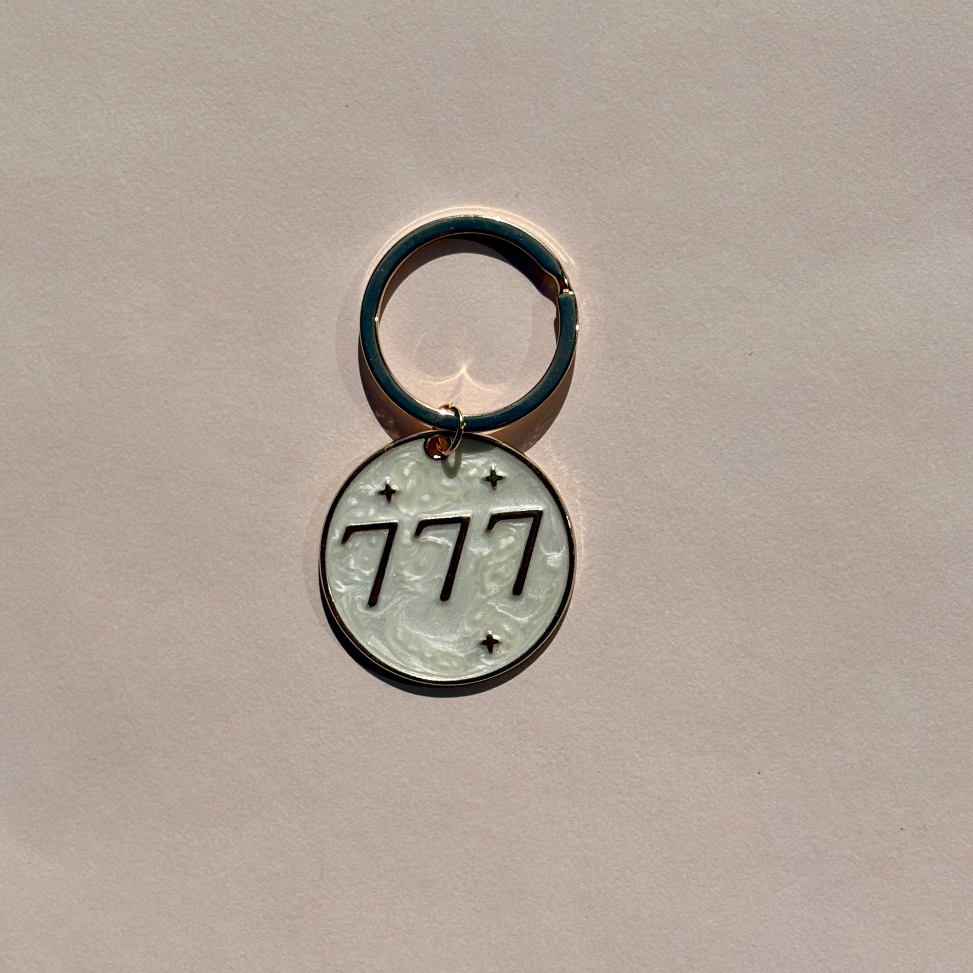 Silver metal keyring engraved with 777 angel number on soft pink background