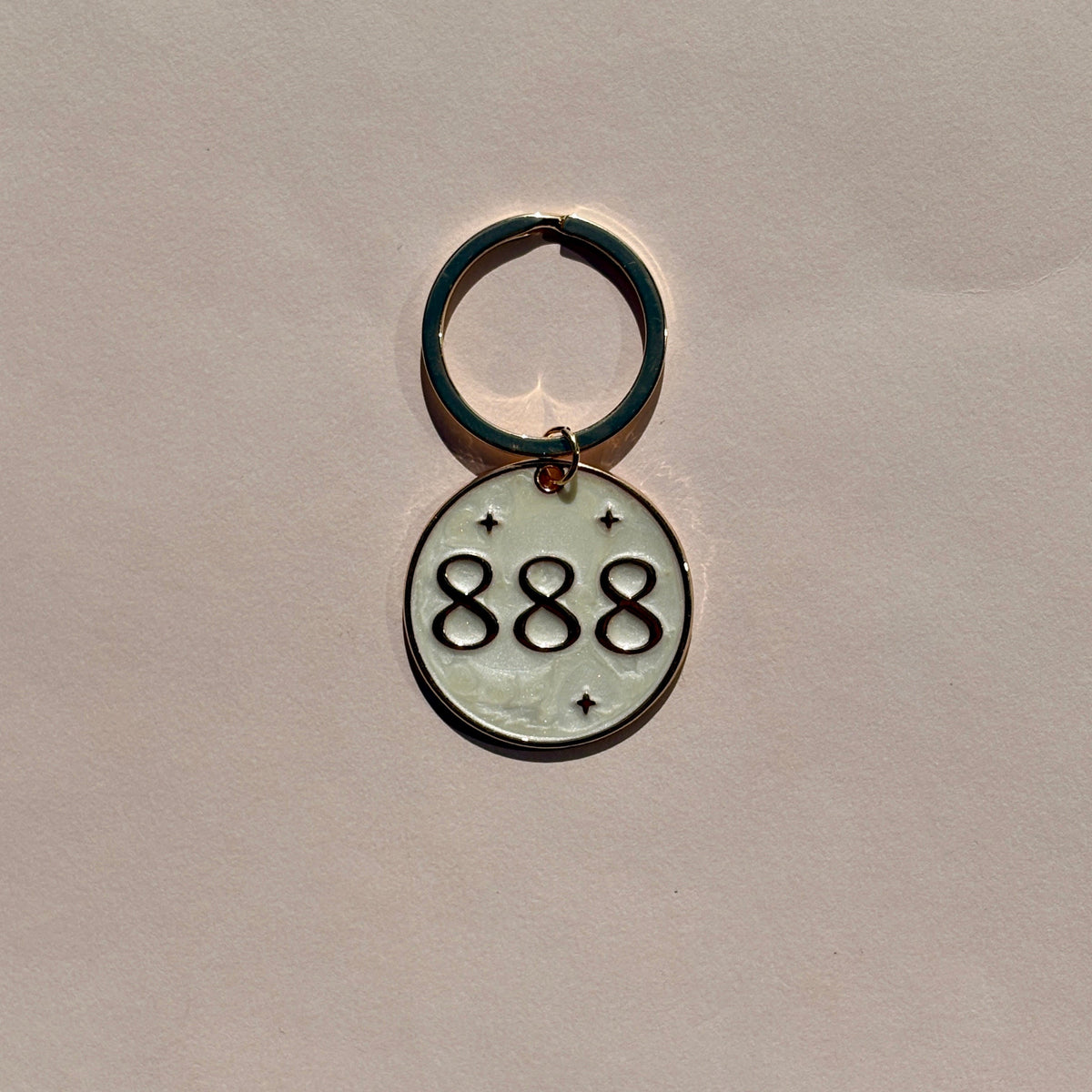 Silver metal keyring engraved with 888 angel number on soft pink background
