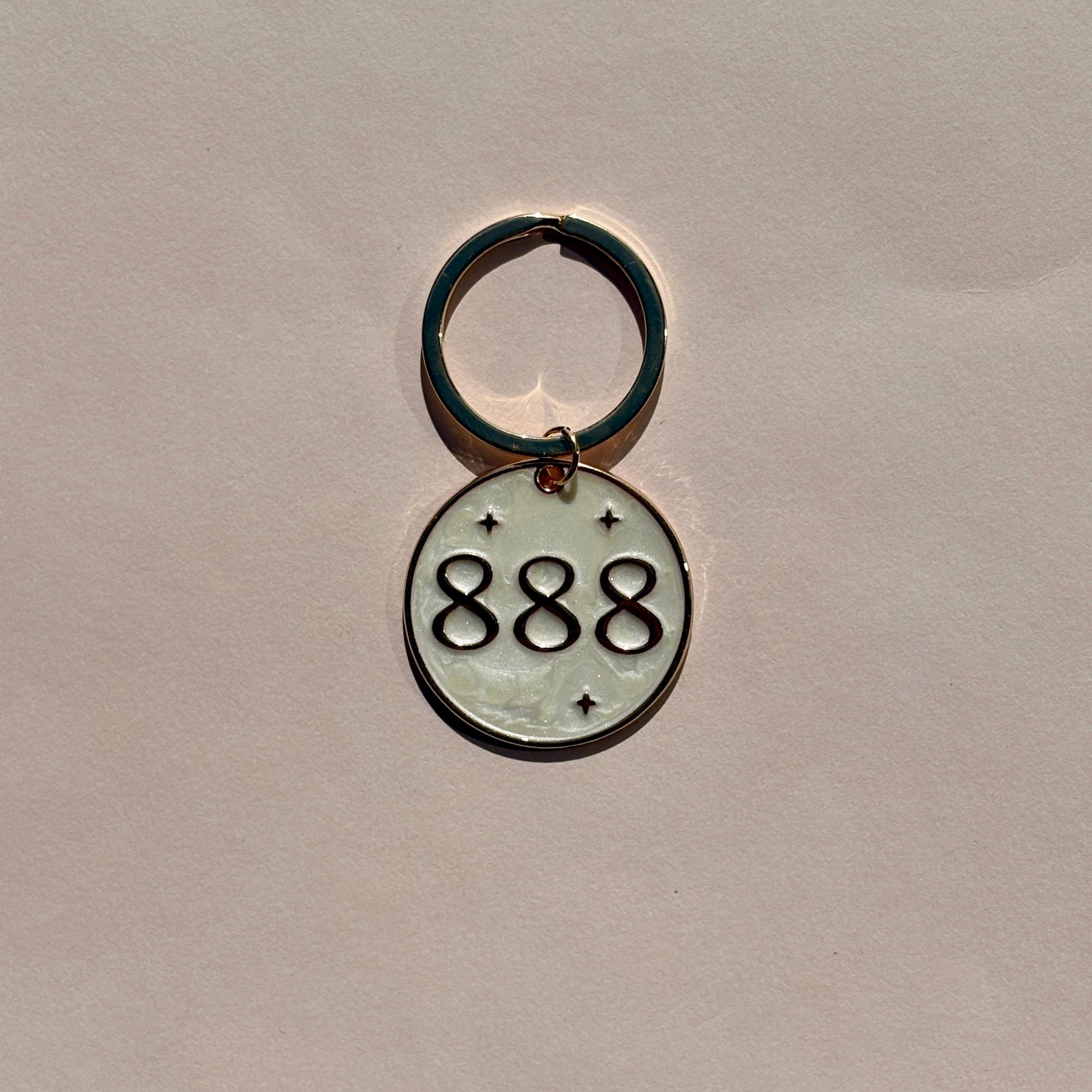 Silver metal keyring engraved with 888 angel number on soft pink background