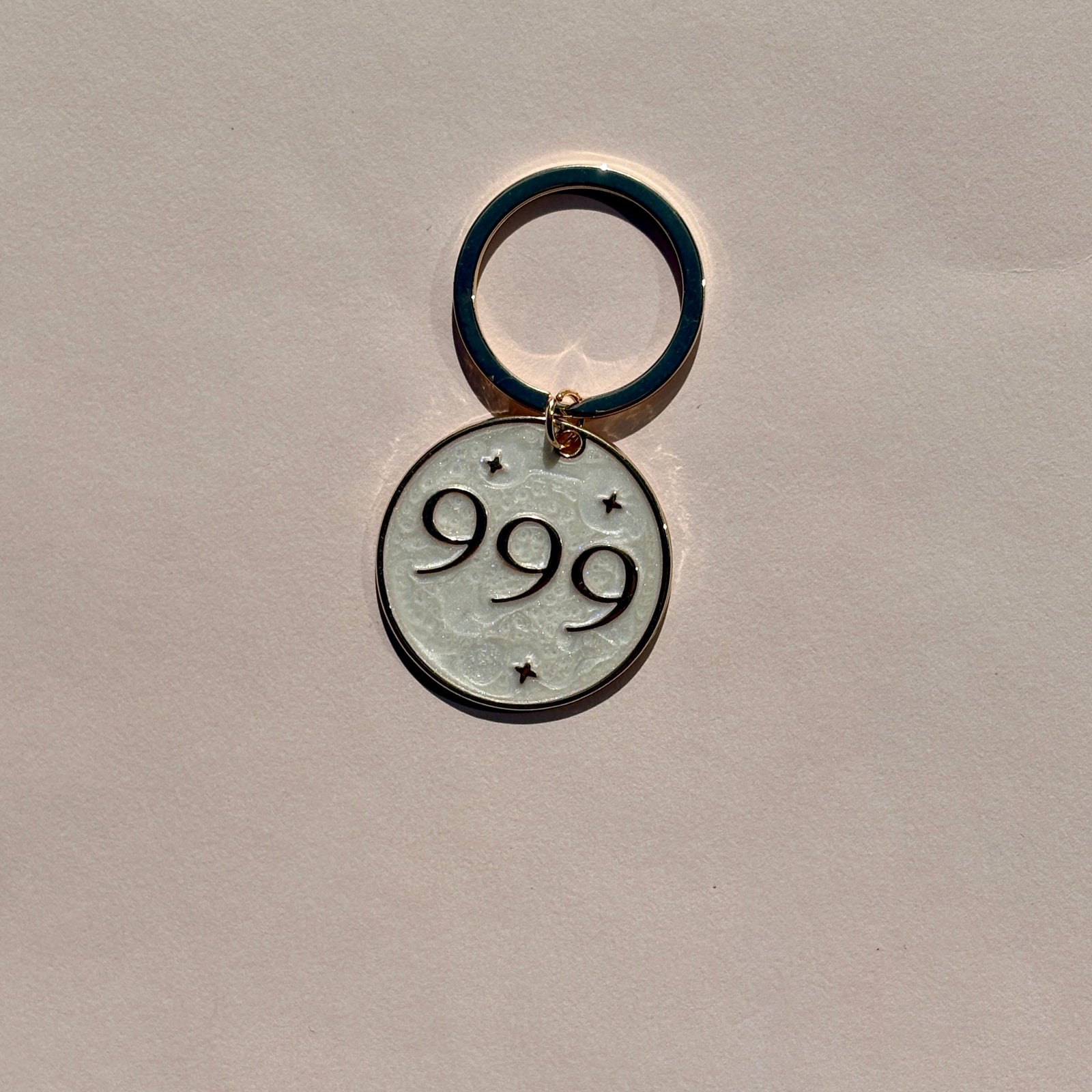 Silver metal keyring engraved with 999 angel number on soft pink background