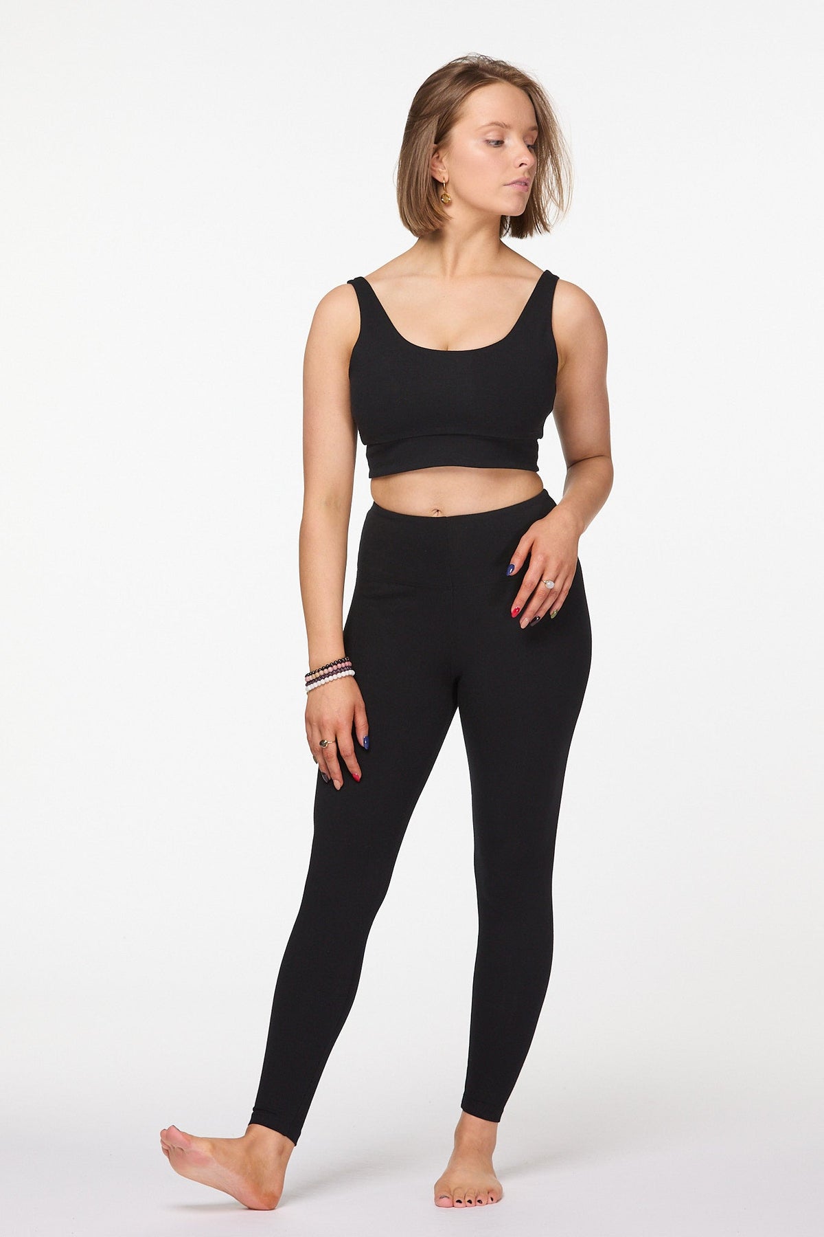 Model wearing black full length high waisted cotton leggings, walking pose on a white background.