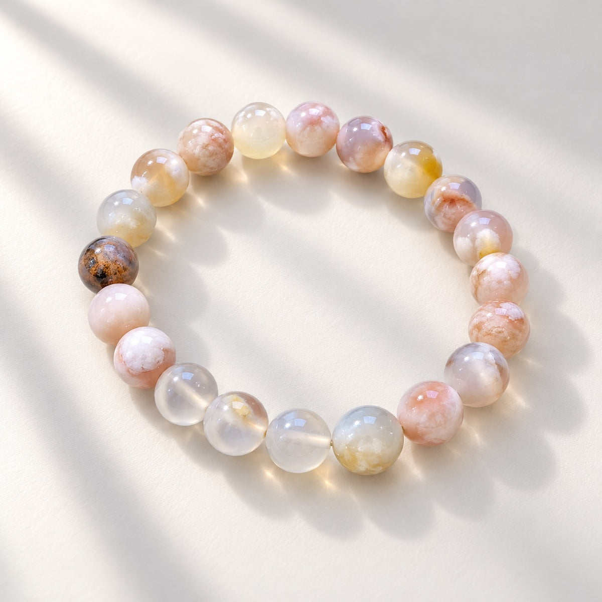 Blossom Agate beaded bracelet arranged in a circle, showing glossy round beads in soft pink, peach, cream, pale yellow and grey.