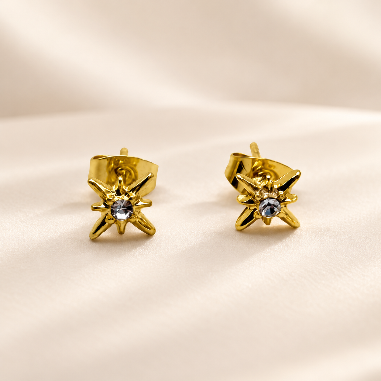Gold starburst stud earrings with clear crystal centre on a soft cream background.