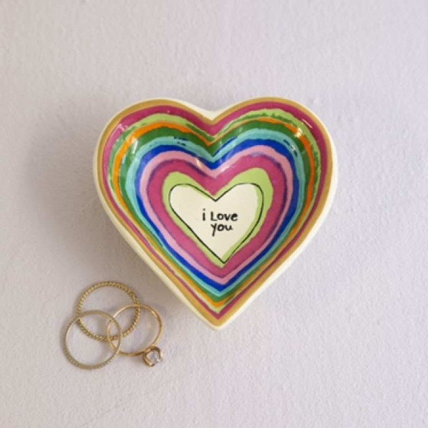 Rainbow coloured Heart-shaped ceramic trinket dish with  text “I love you”, holding gold rings on a white surface