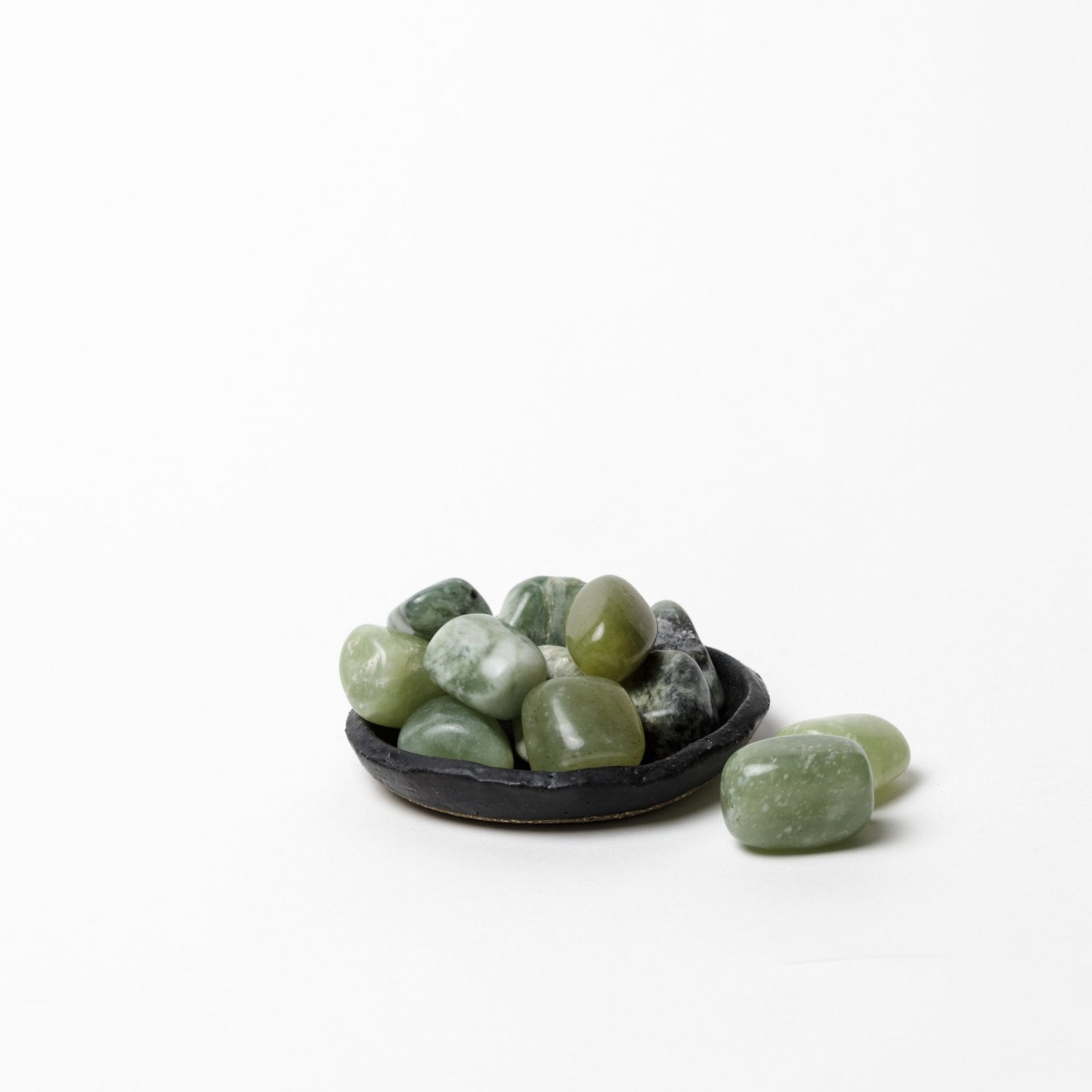 Polished green jade tumble stones in small black dish on white background