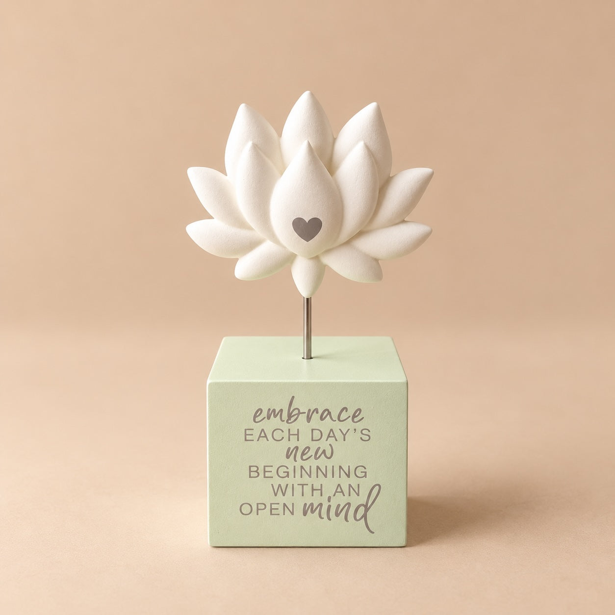 Cream lotus flower figure with layered petals and a small heart, raised on a slim metallic coloured stem above a pale green square base with an inspirational message.