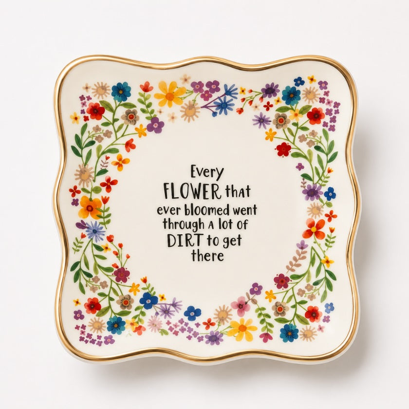 White ceramic trinket bowl with colourful floral border, gold rim detail and inspirational “Every flower that ever bloomed went through a lot of dirt to get there” quote in the centre.