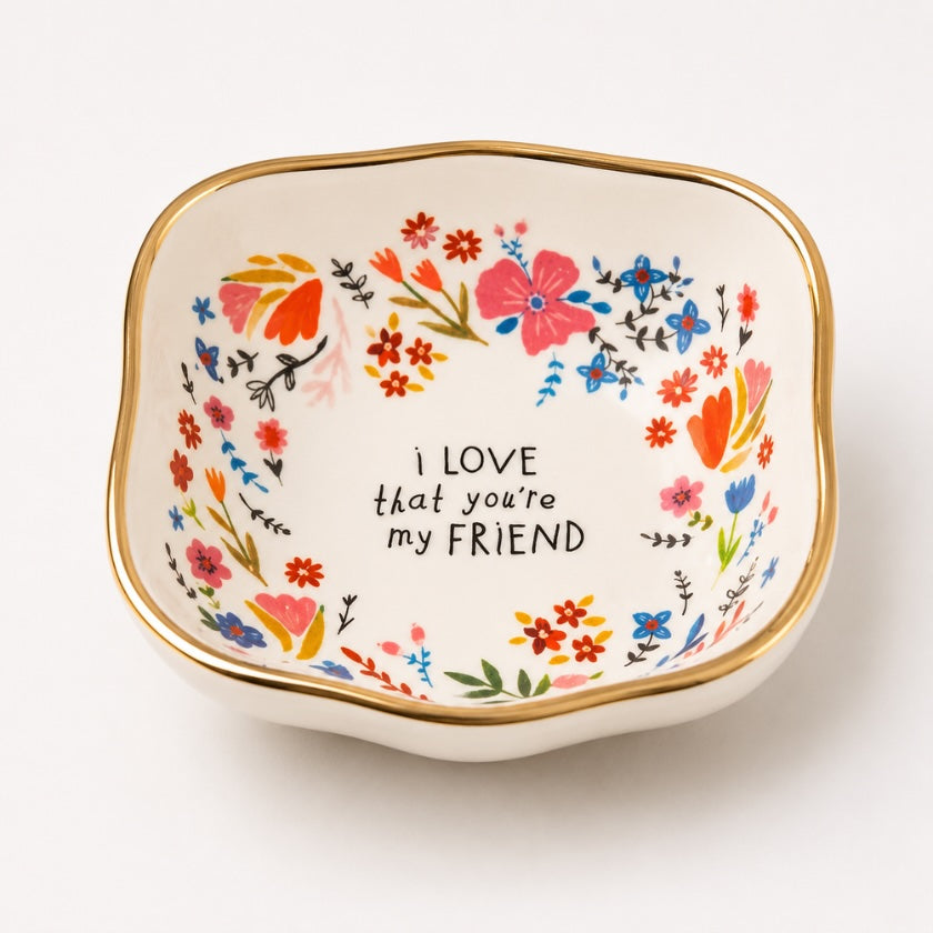 White ceramic trinket bowl with colourful floral illustrations, gold rim detail and “I love that you’re my friend” quote in the centre.