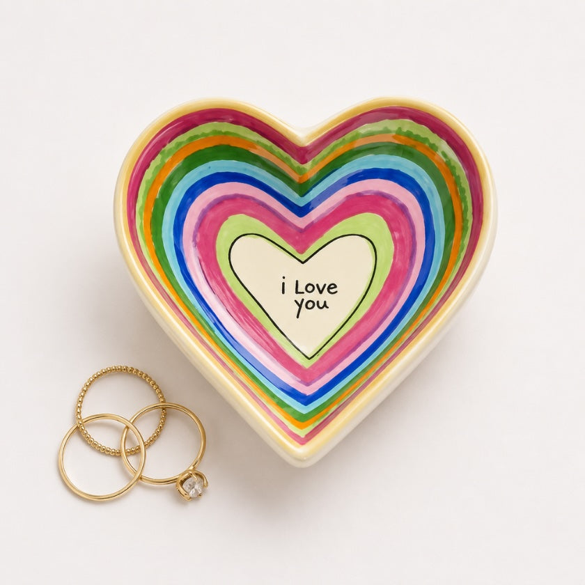 Heart shaped ceramic trinket bowl with colourful rainbow heart design and “I Love You” quote in the centre, styled with gold rings on a neutral background.