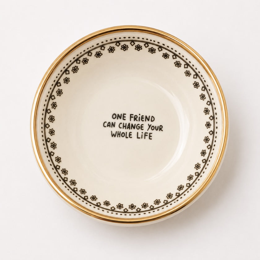 White ceramic trinket bowl with gold rim and delicate floral border pattern featuring “One friend can change your whole life” quote in the centre.