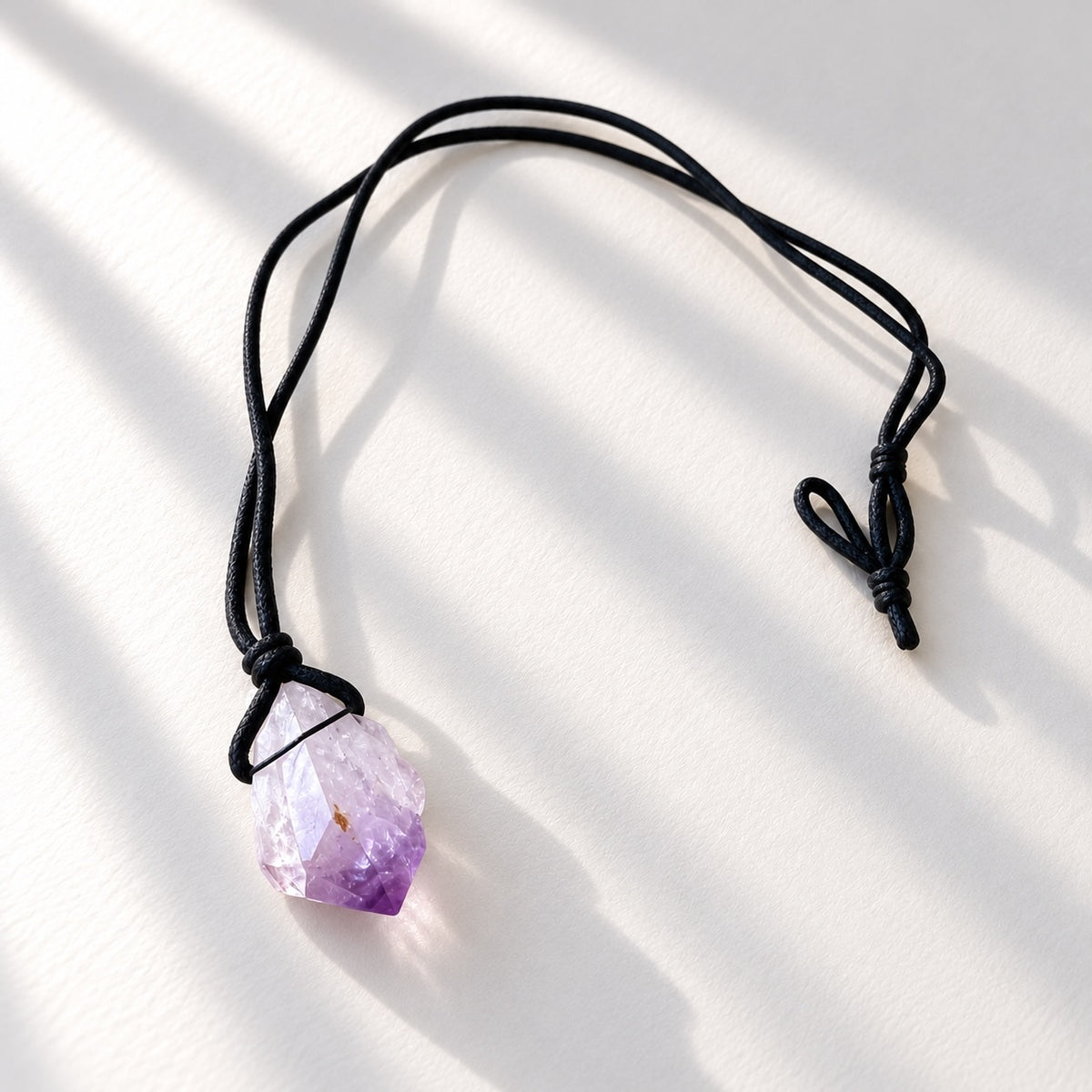 Natural raw amethyst crystal pendant tied onto a simple black cord necklace.