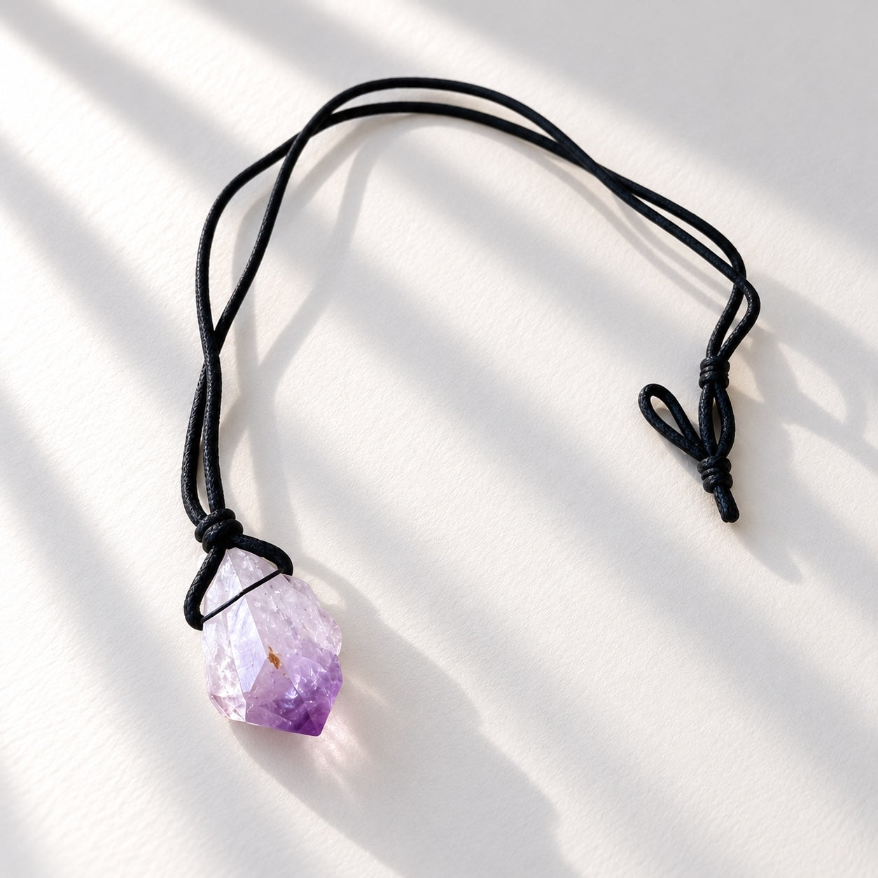 Natural raw amethyst crystal pendant tied onto a simple black cord necklace.