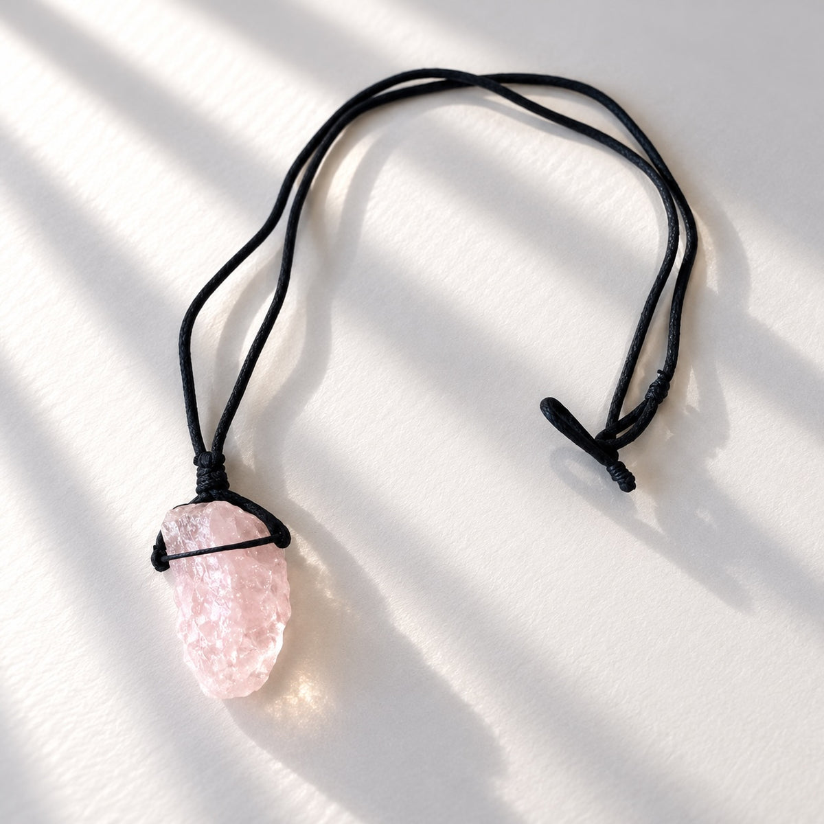 Natural rough rose quartz crystal pendant on black cord necklace.