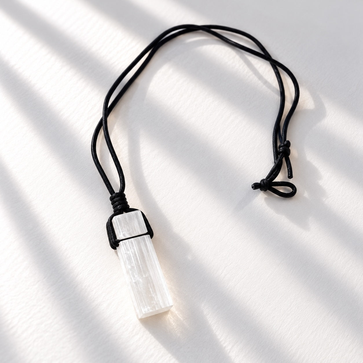 Natural raw selenite crystal pendant suspended from an adjustable black cord necklace.
