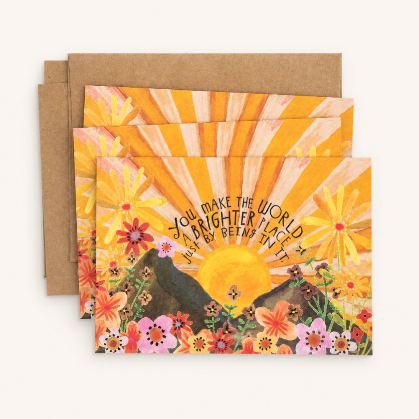 Sunshine themed greeting card with floral landscape illustration and “You make the world a brighter place just by being in it” quote.