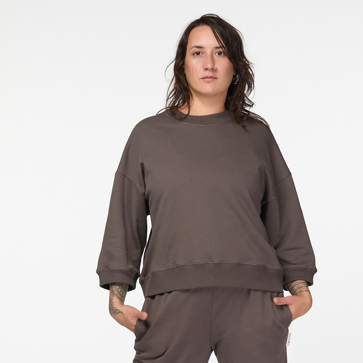 Woman wearing oversized brown organic cotton jumper with cropped sleeves on white background