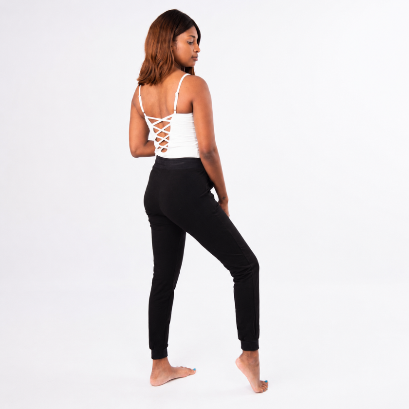 Model wearing the Luna &amp; Soul white zigzag strap top with crisscross back detail and black organic cotton jogger pants, shown from the back on a clean studio background