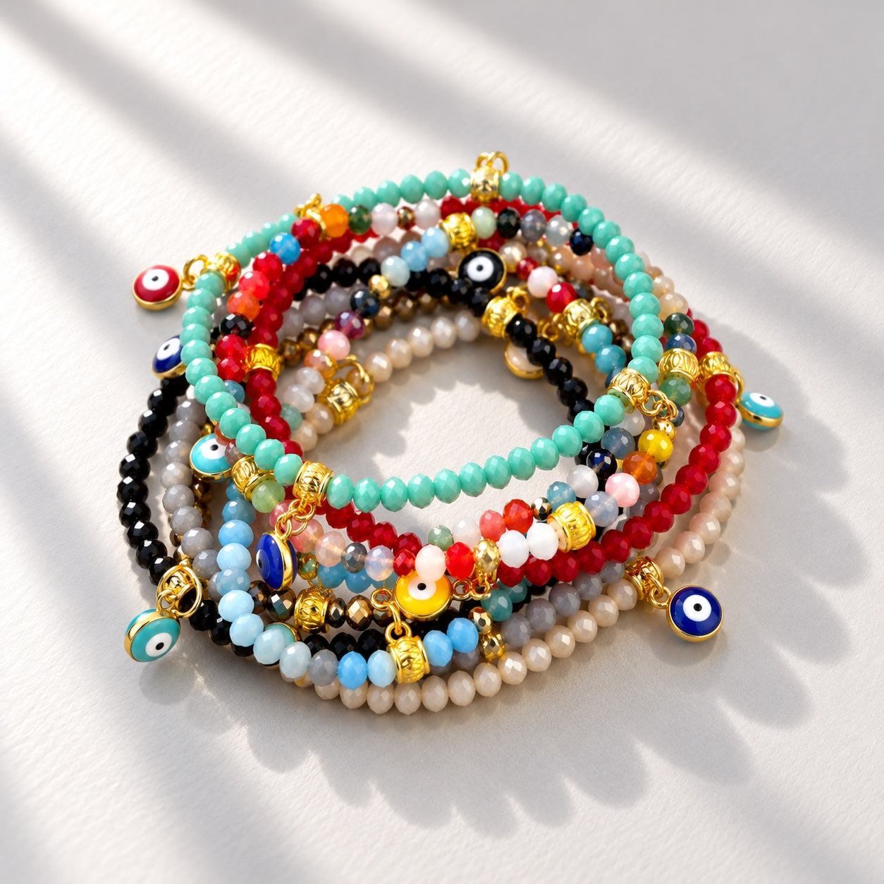 Stack of colourful faceted beaded evil eye bracelets with turquoise, red, blue, black and neutral beads, gold toned accents and dangling mati charms.