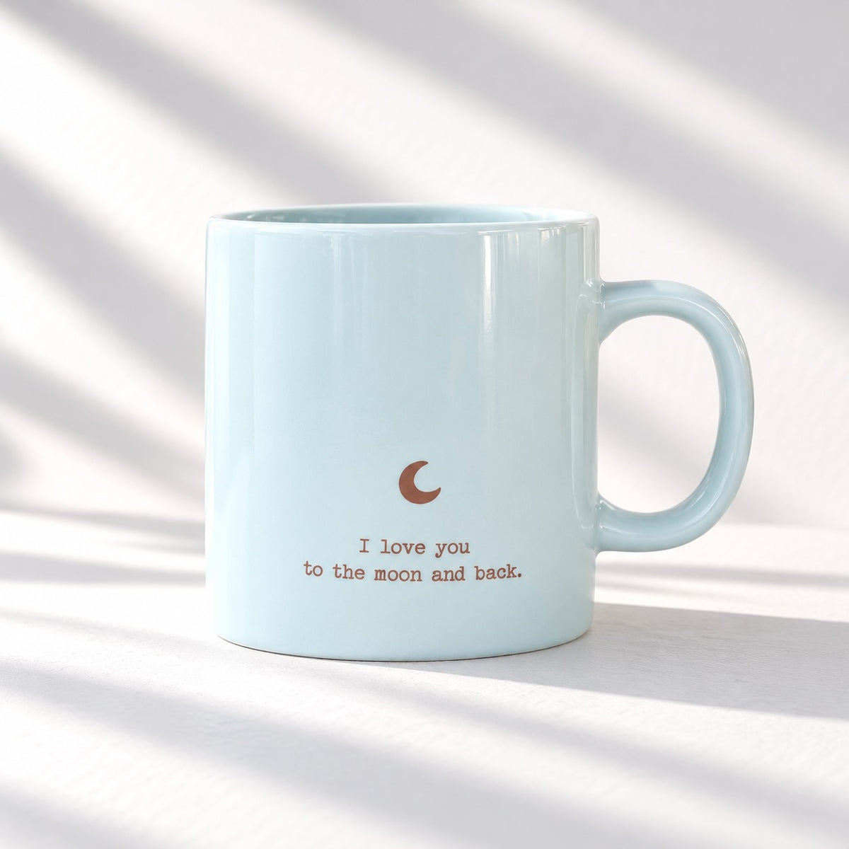 Pale blue glossy mug with a crescent moon and “I love you to the moon and back” foil lettering, front view on a white background.
