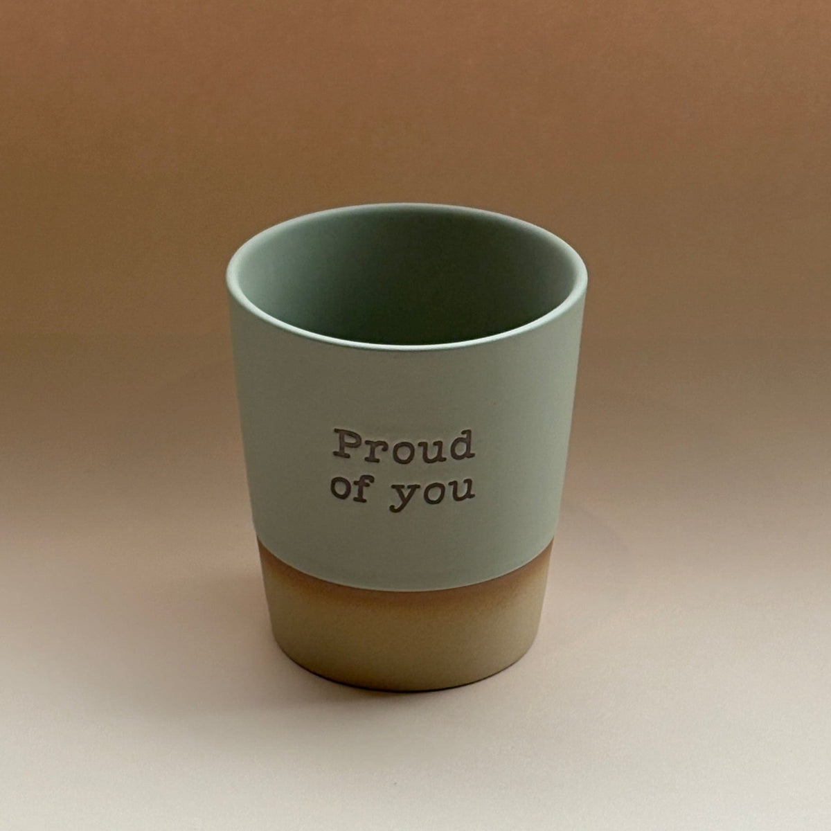 Green cup with &#39;Proud of you&#39; text on a beige background