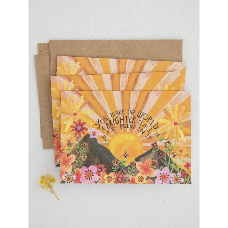 Greeting card with sun and floral design reading “You make the world a brighter place just by being in it” on white background