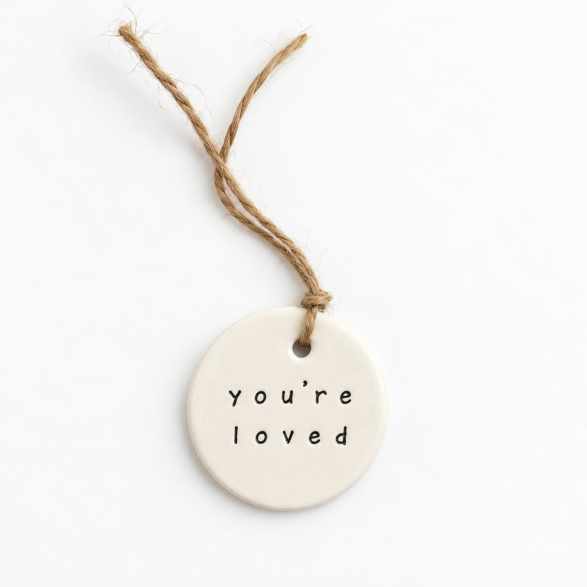 Cream handmade ceramic hanging tag stamped “You’re Loved”, with natural jute twine, on a white background.